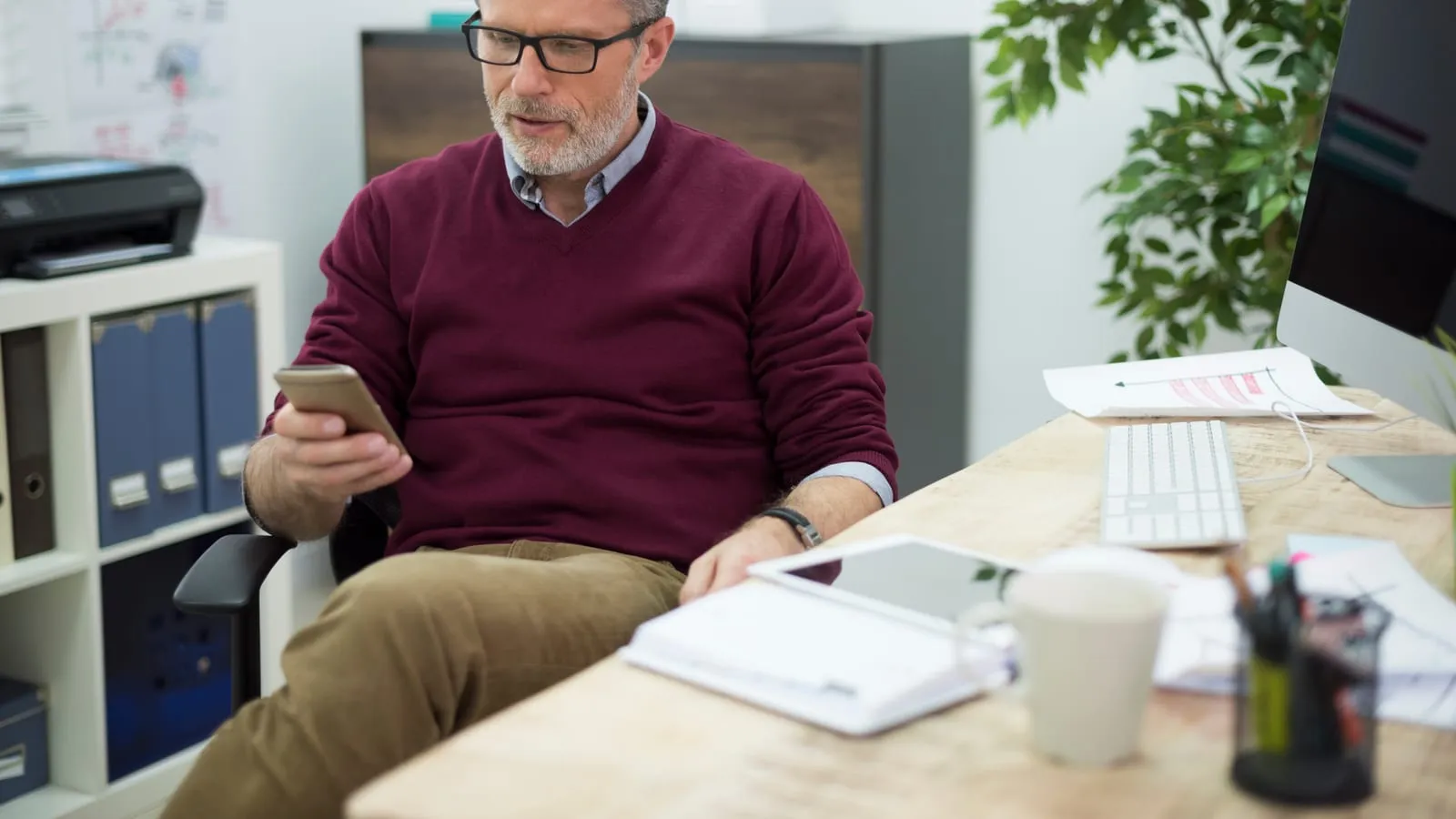Gestor comercial olhando mensagens de clientes no celular, sentado à mesa do escritório